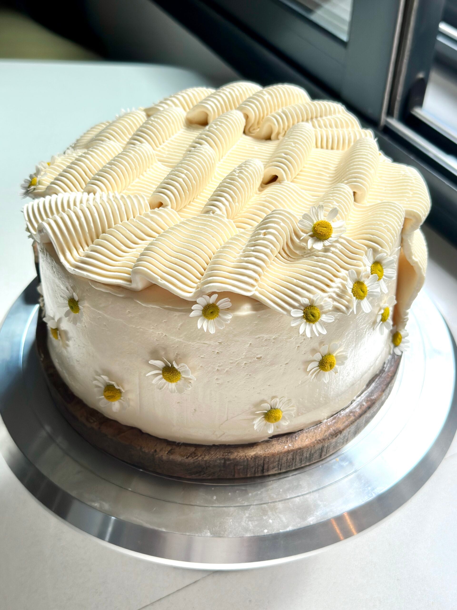 Frosted two layer banana cake with rippled frosting and edible flowers.