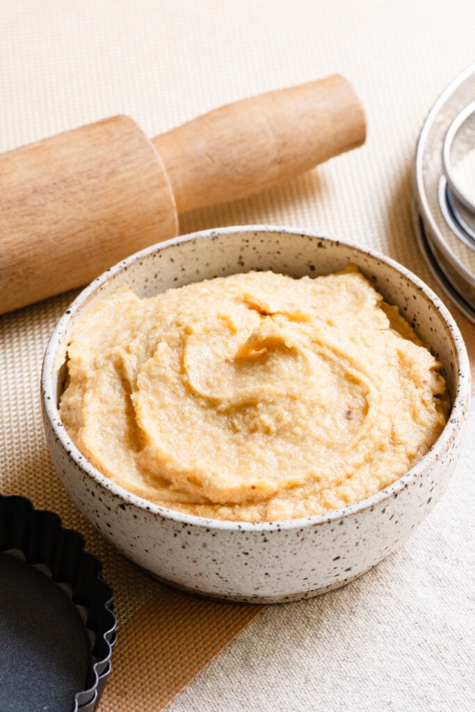 Bowl of French almond cream next to a rolling pin and tart pan.