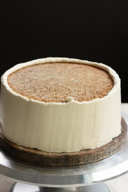 Partially frosted two layer cake with honey buttercream on a turntable.