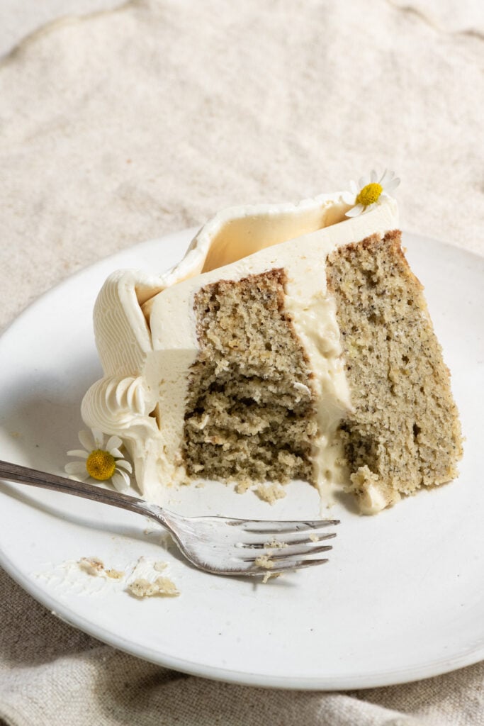 Slice of banana layer cake partially eaten on a plate with a fork.