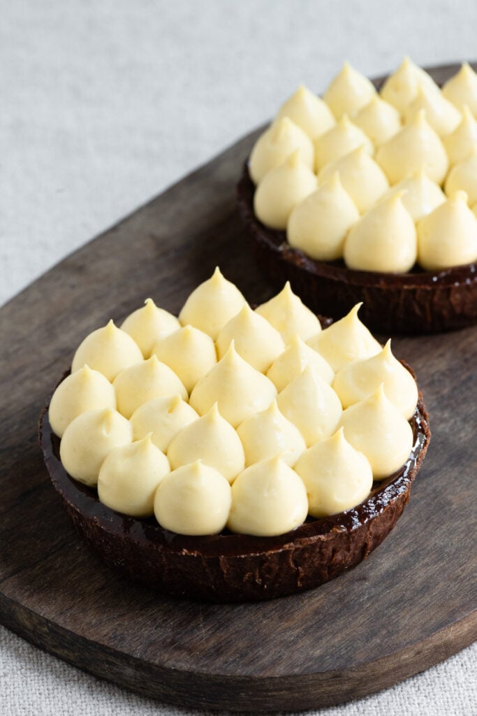 Banana cremeux piped onto chocolate tarts on a wood board.