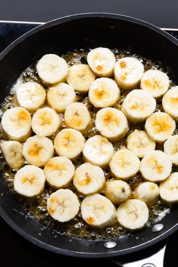 Banana sliced cooking in a pan with butter and brown sugar.