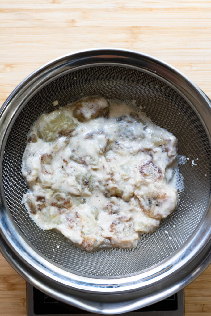 Cream soaked bananas in a metal sieve.