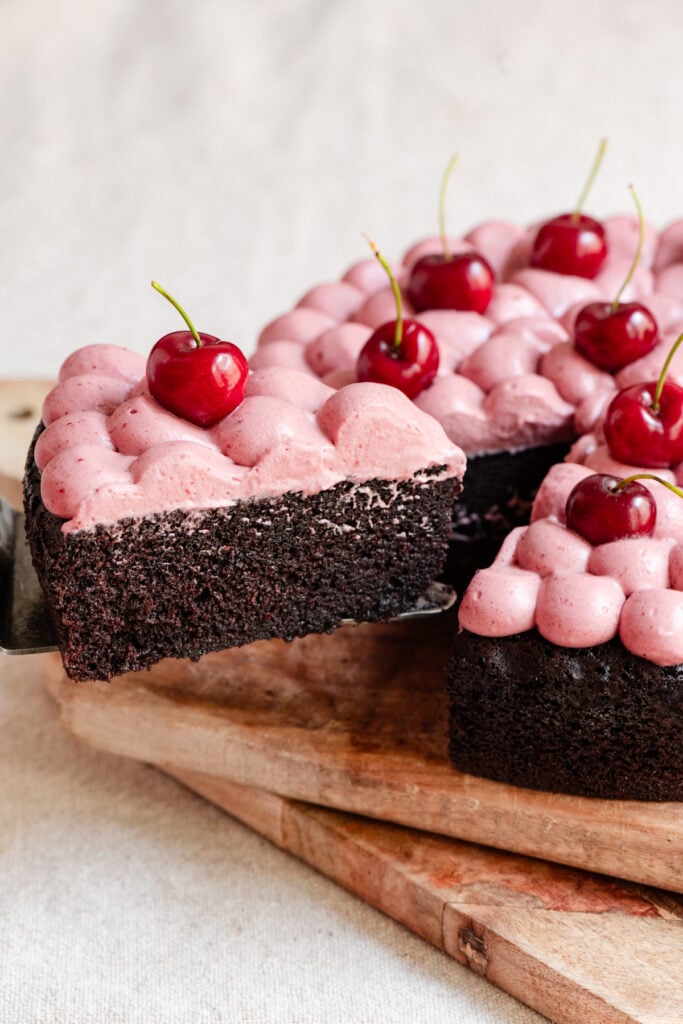 Slice of chocolate olive oil cake topped with cherry ganache and fresh cherries pulling away from the whole cake.