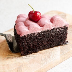 Slice of chocolate olive oil cake topped with cherry ganache on a serving board.