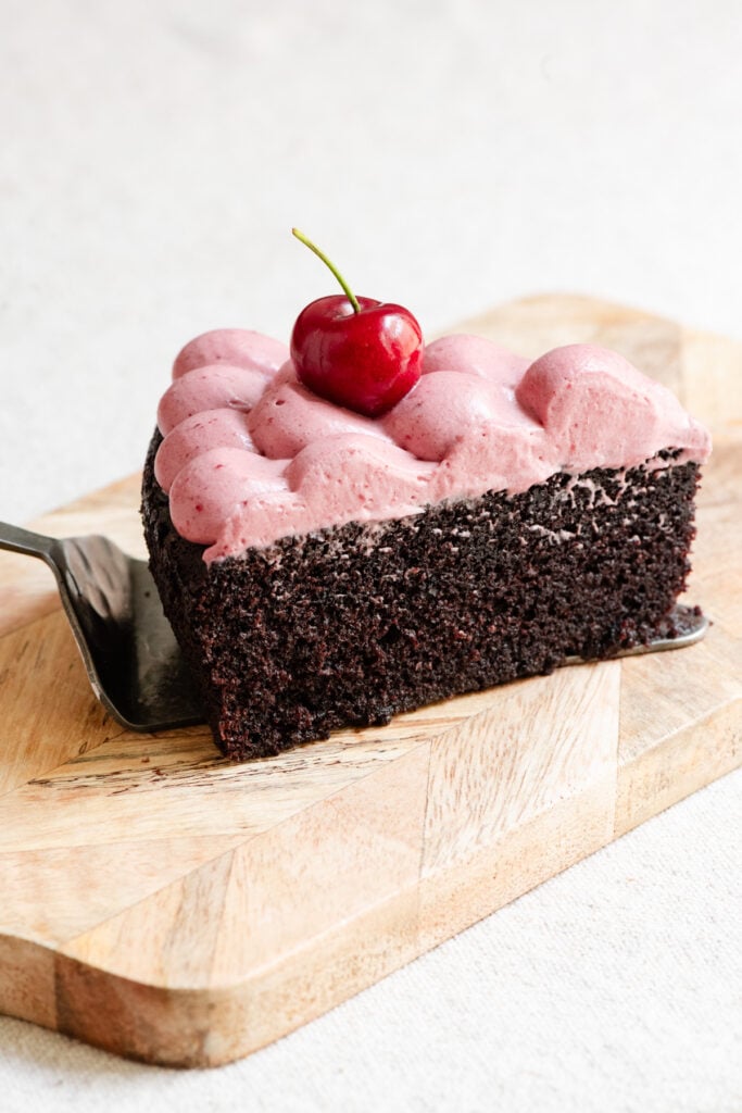 Slice of chocolate olive oil cake topped with cherry ganache on a serving board.