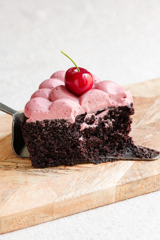 Partially eaten slice of chocolate olive oil cake with cherries.