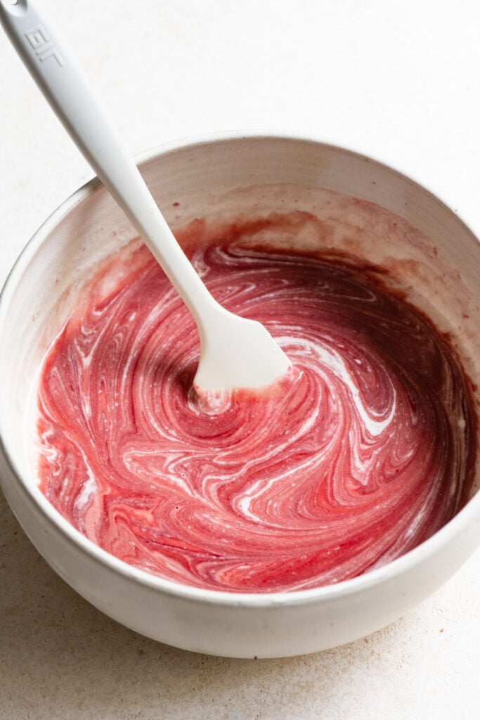 Cream being stirred into melted raspberry chocolate.