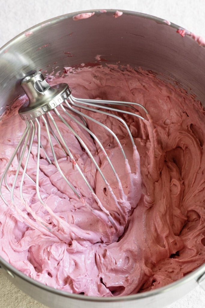 Whipped cherry ganache in the bowl of a stand mixer with whisk attachment.
