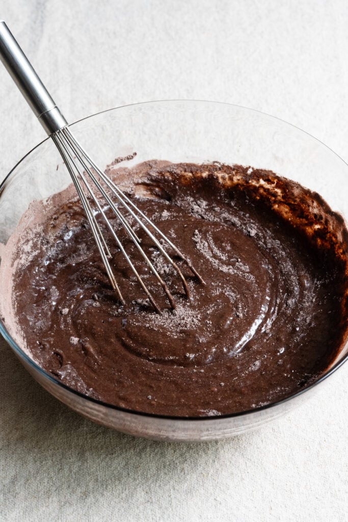 Whisk in a bowl with chocolate cake batter.