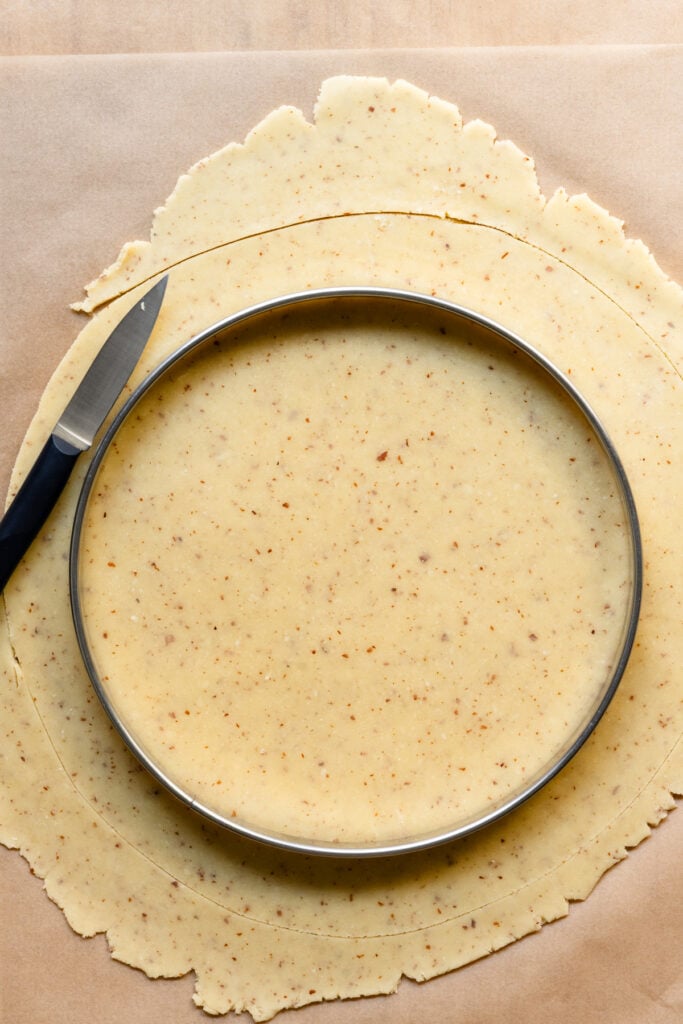 Overhead of a tart ring on top of tart dough being cut to fit.