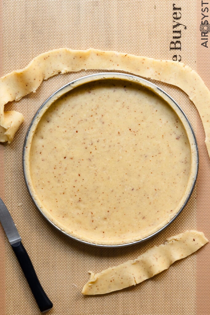 Overhead of a tart ring lined with pastry dough and excess dough cut away.