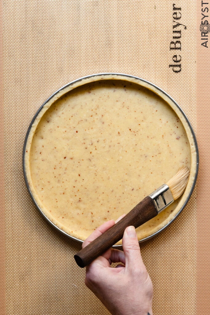 Overhead of a hand pressing tart dough into a pastry ring with a pastry brush.