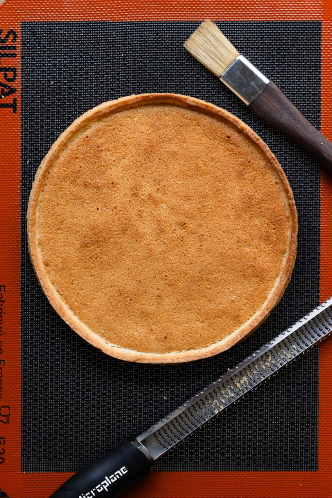 Overhead of a baked tart with almond cream filling next to pastry tools.