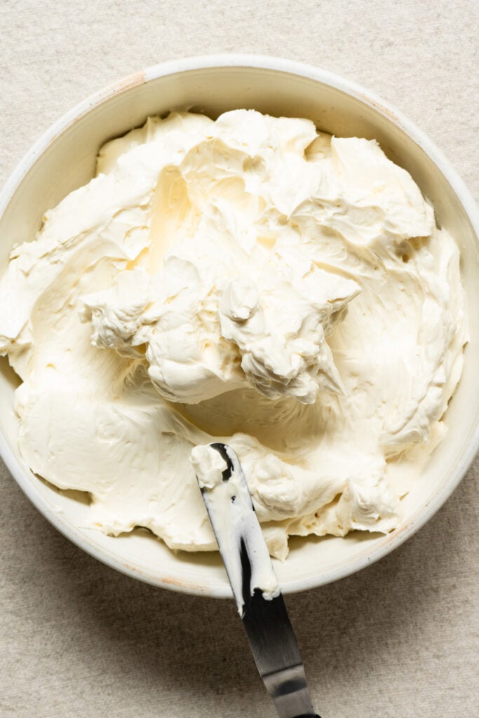 Overhead of honey Swiss meringue buttercream in a bowl with a spatula.