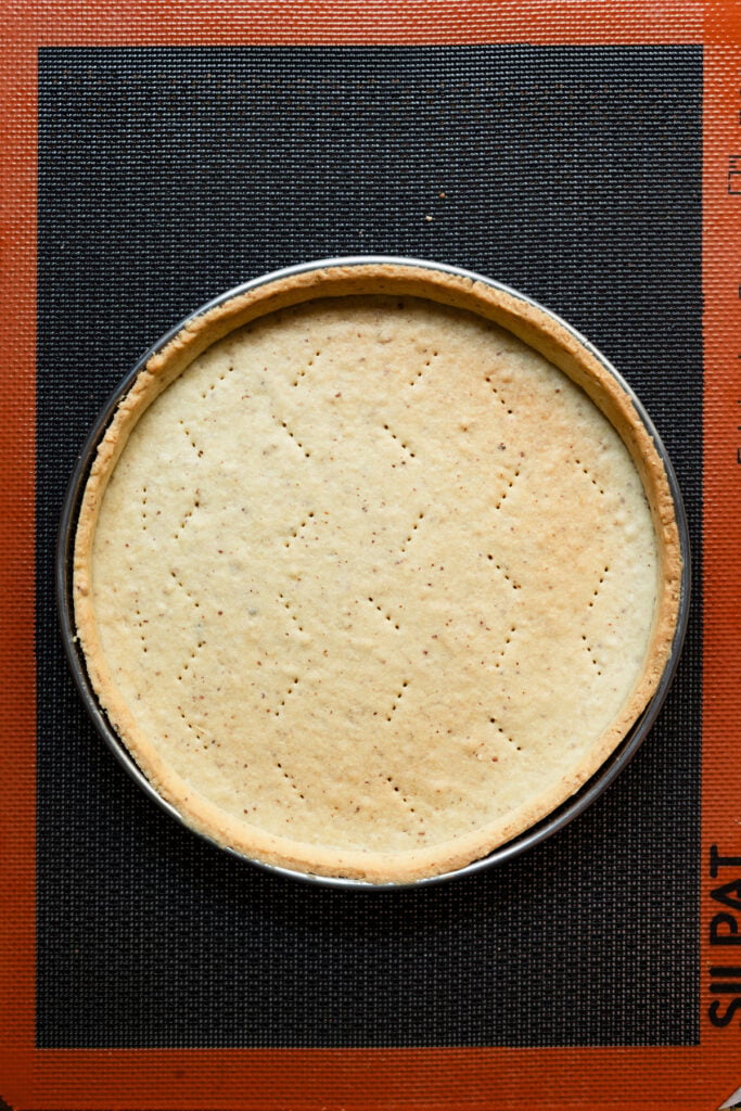 Overhead of a partially baked tart shell on a baking mat.