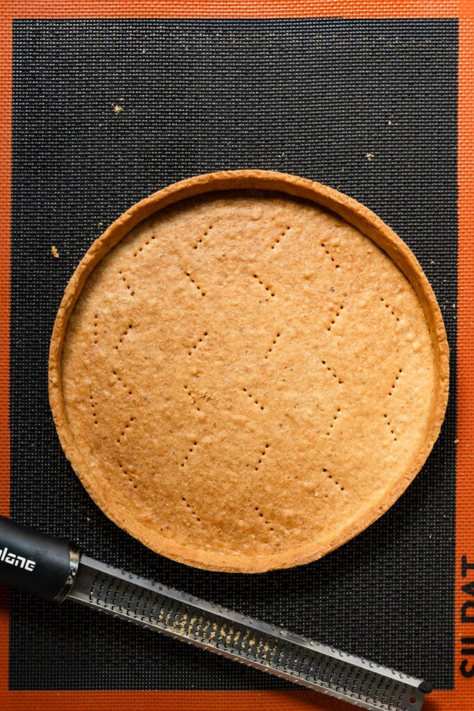 Overhead of a baked pate sucree tart crust next to a micropane.