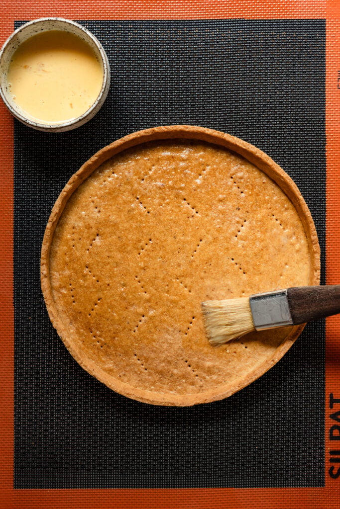 Pastry brush adding egg wash to a baked tart shell.