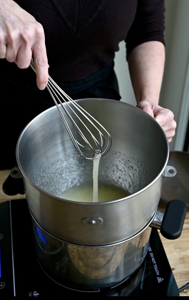 Double broiler with saucepan and mixing bowl. Person whisking egg white sin the double broiler bowl.