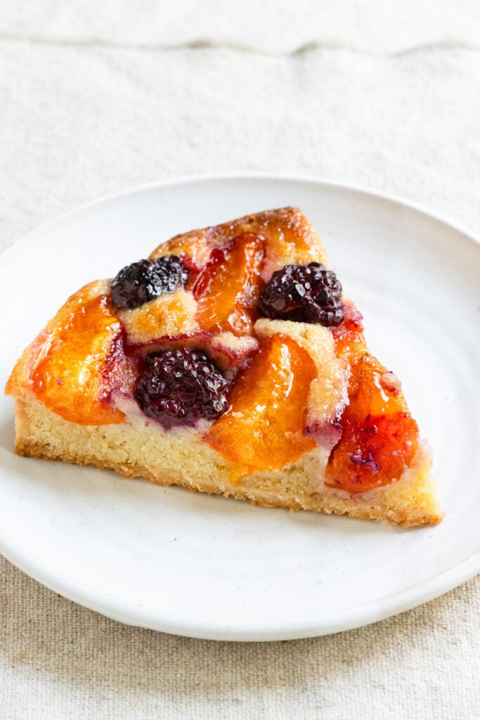 Slice of French apricot and blackberry tart on a plate.