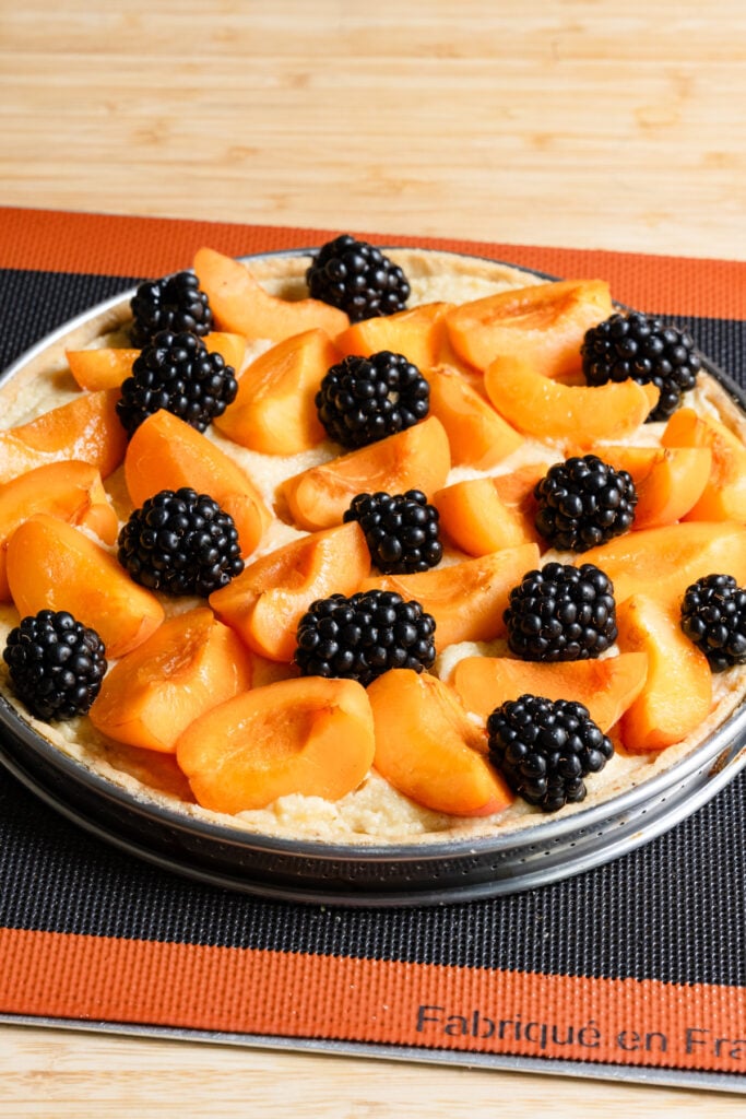 Unbaked tart filled with almond cream and topped with apricots and blackberries on a baking tray.