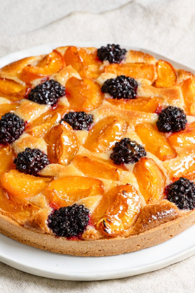 Apricot and blackberry tart coated with apricot glaze on a plate.