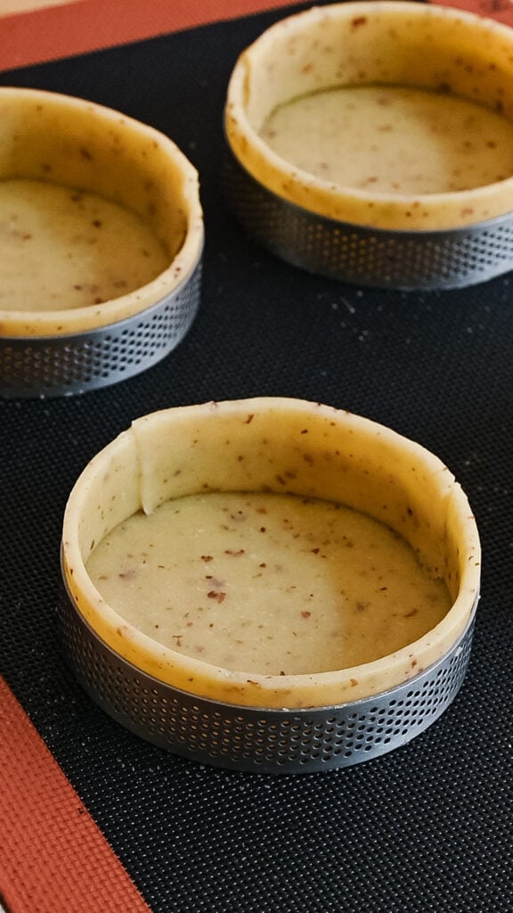 Lined tart rings with pastry dough on a baking pan.
