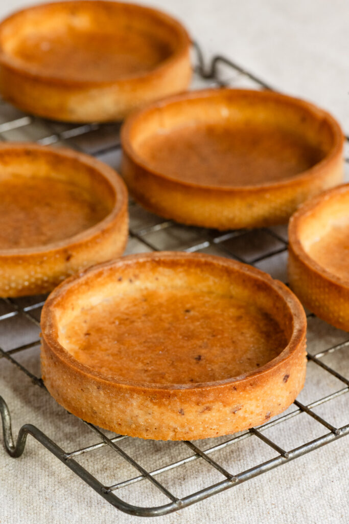 Baked empty tartlet shells on a wire rack.