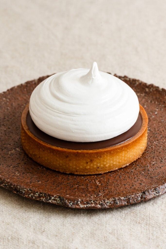 Tartlet filled with chocolate ganache and topped with meringue on a plate.