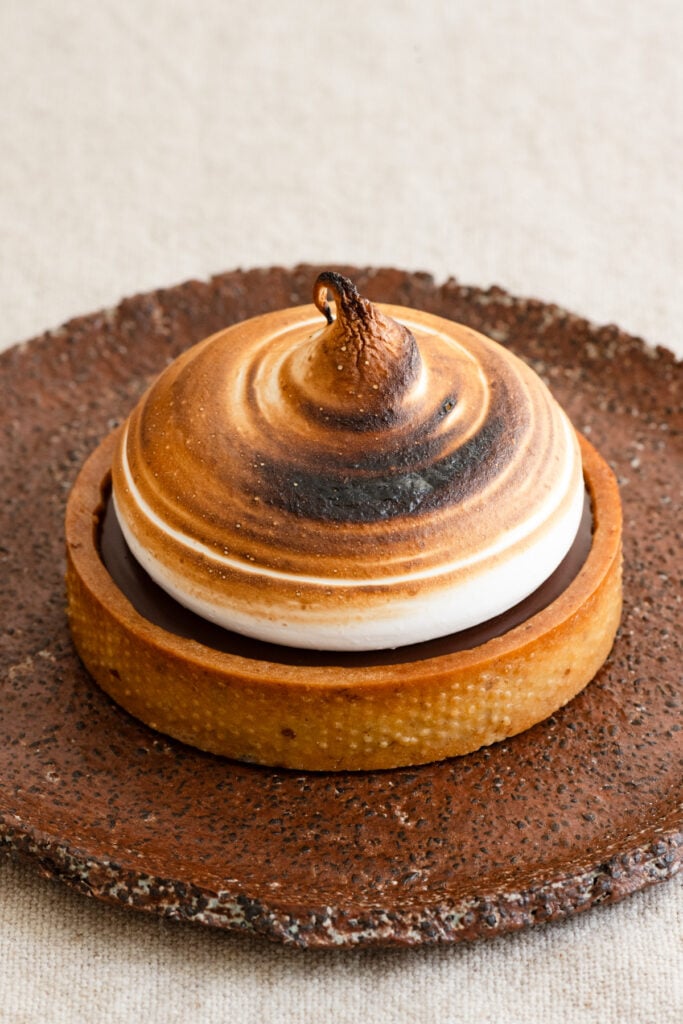 Toasted meringue topped chocolate tartlet on a plate.