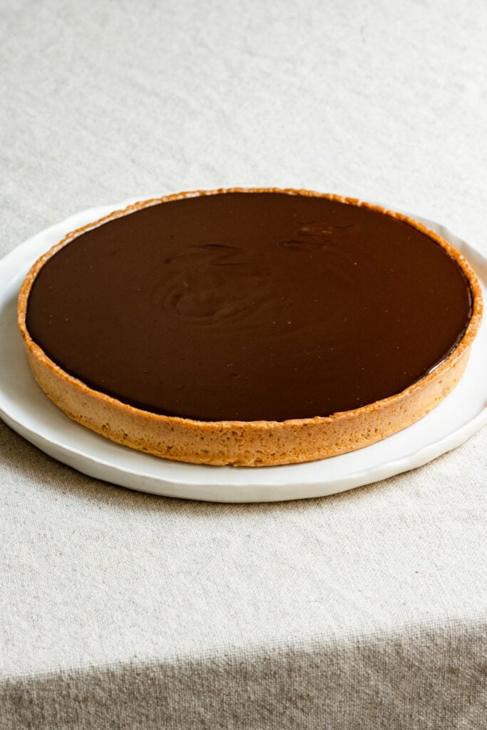 Tart shell filled with chocolate ganache on a round plate.