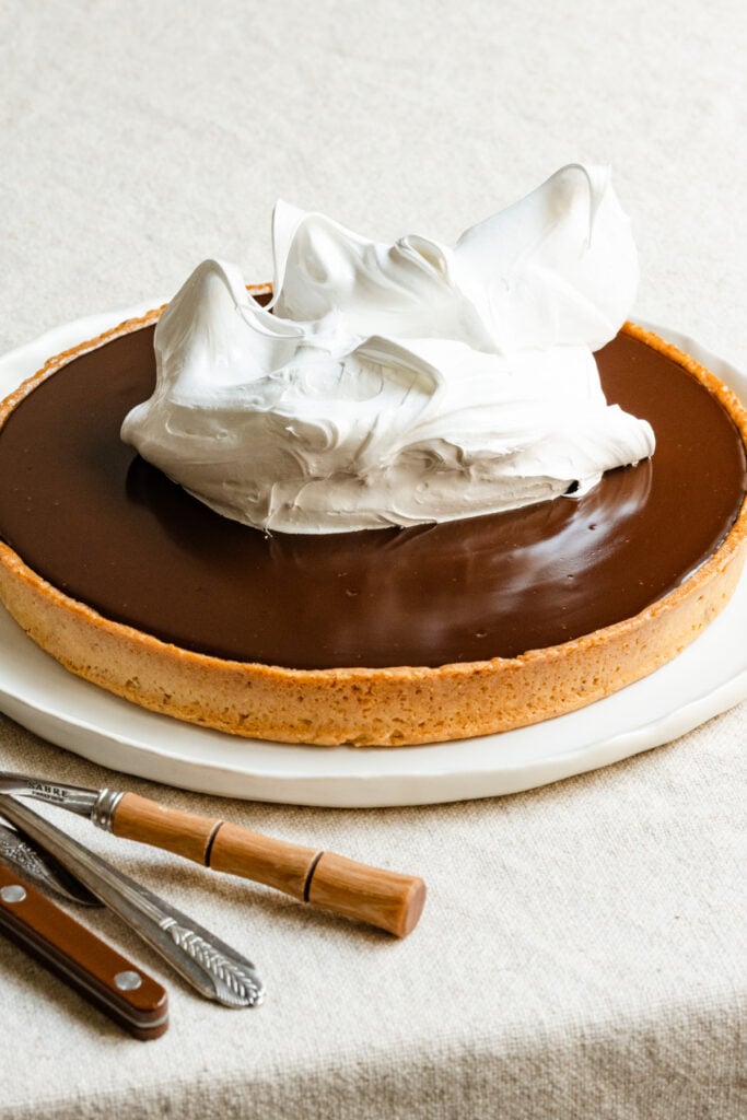 Stiff peak meringue spooned onto a chocolate tart on a serving plate.