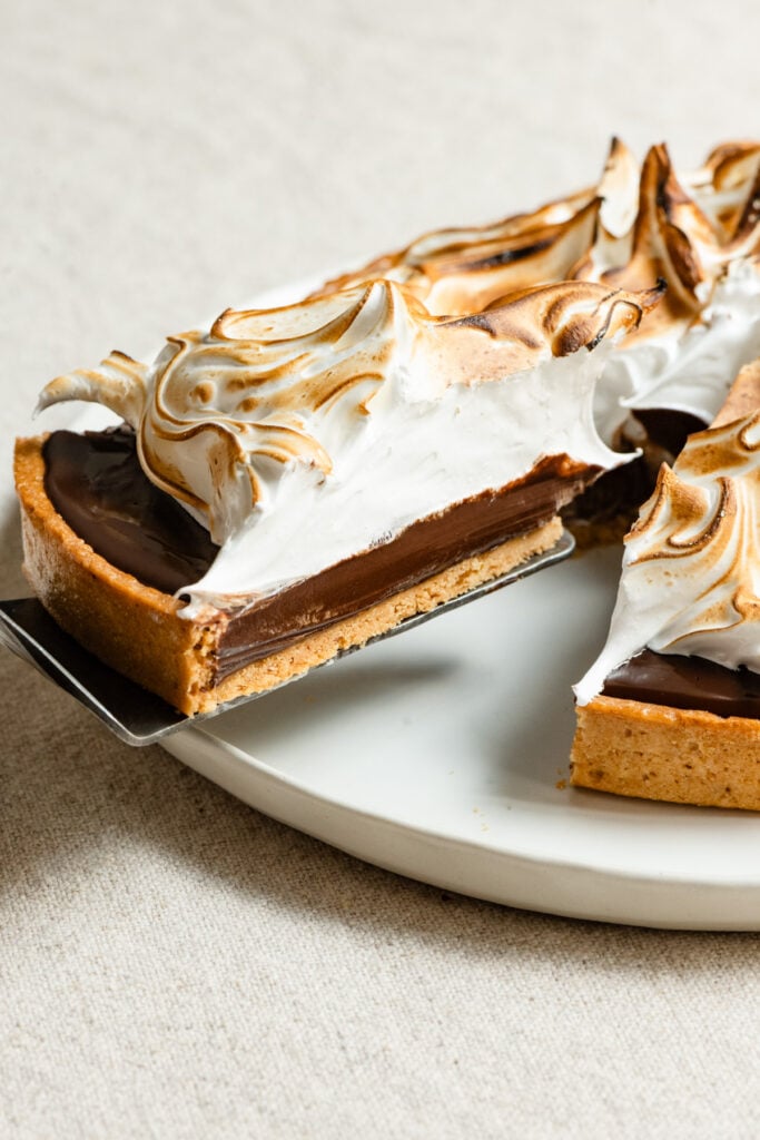 Slice of s'mores tart being lifted form the whole tart on a plate.