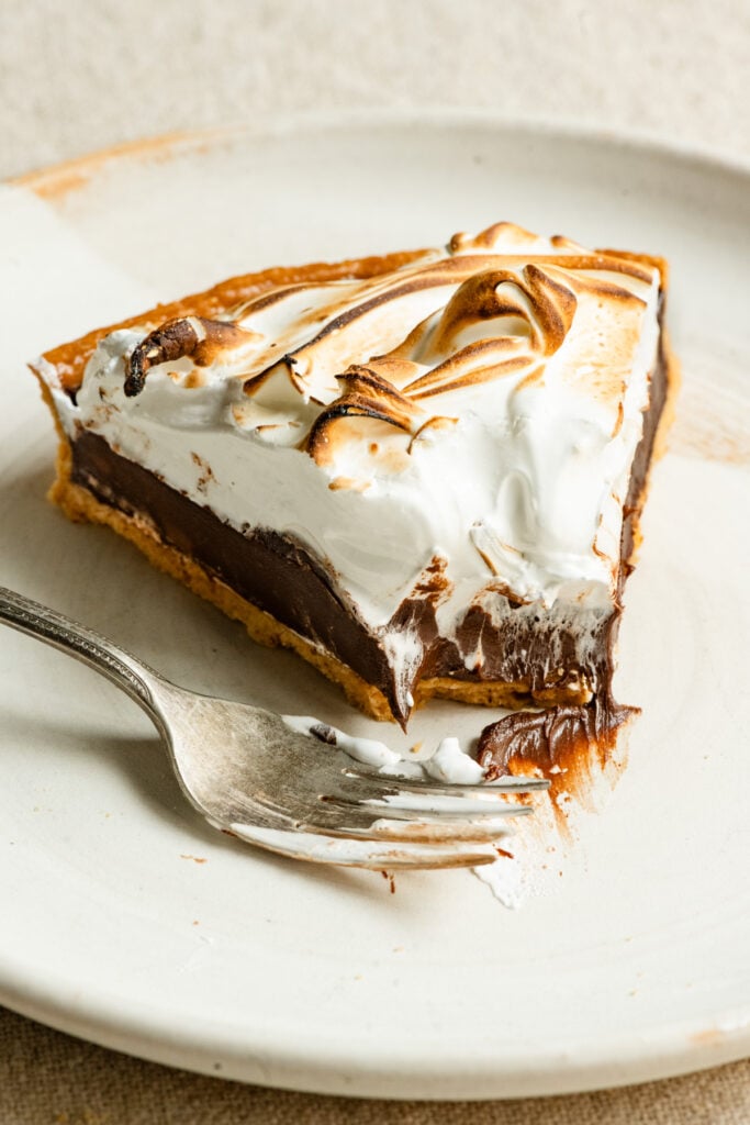 Slice of chocolate meringue tart partially eaten on a plate next to a fork.