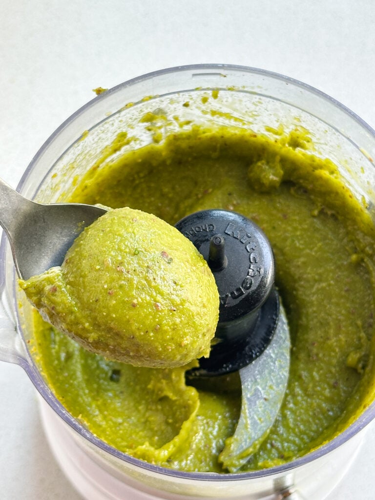 Spoon scooping raw pistachio paste from a blender.