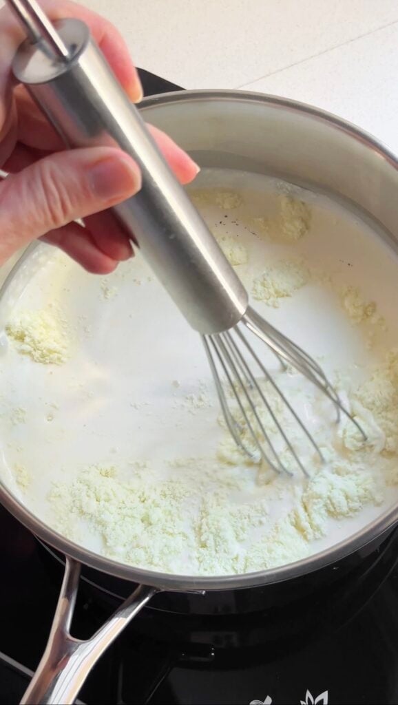Hand whisking skim milk powder into a pot of cream.