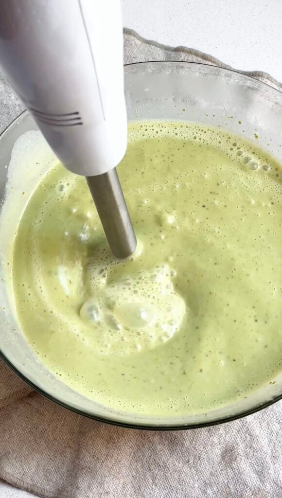 Pistachio ice cream mixing with a stick blender in a large glass bowl.