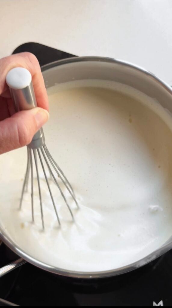 Stirring ice cream base with a whisk in a pot.