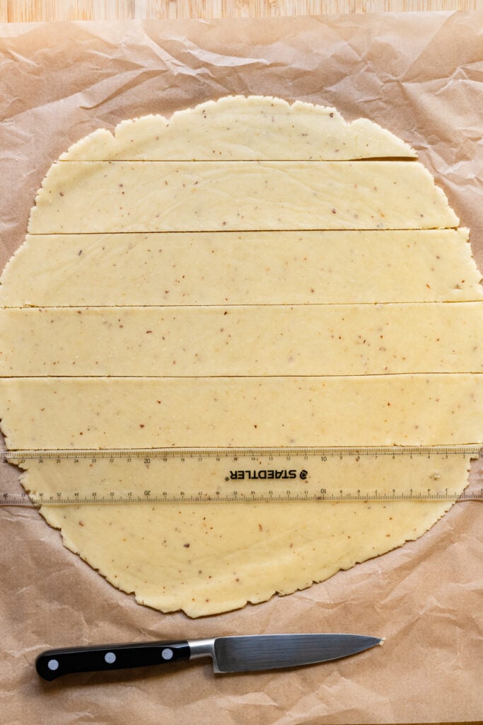 Overhead of a ruler measuring strips of rolled out dough.