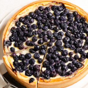 Overhead of a slice of blueberry topped flan tart being pulled away with a pie server.