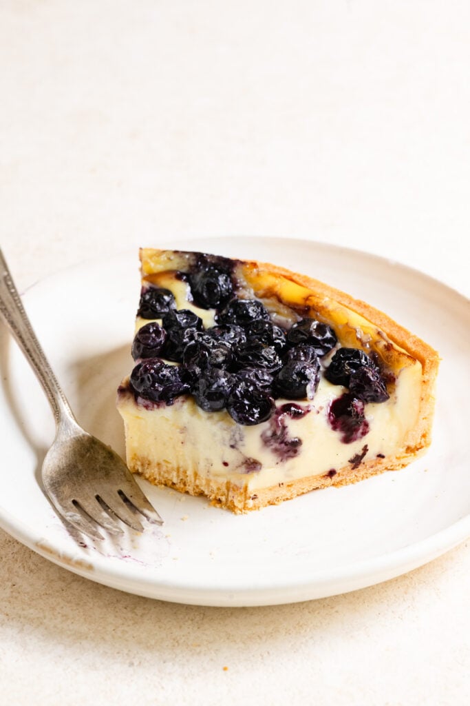 Slice of French flan topped with blueberries and a bite missing.