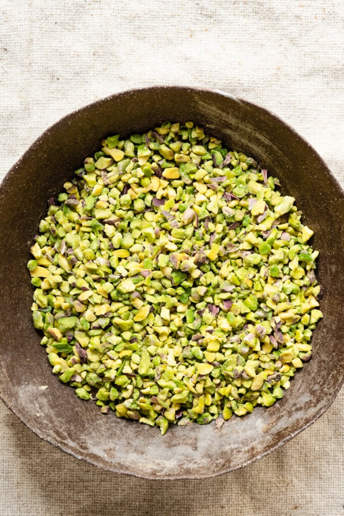 Overhead of a bowl filled with chopped raw green pistachio nuts.