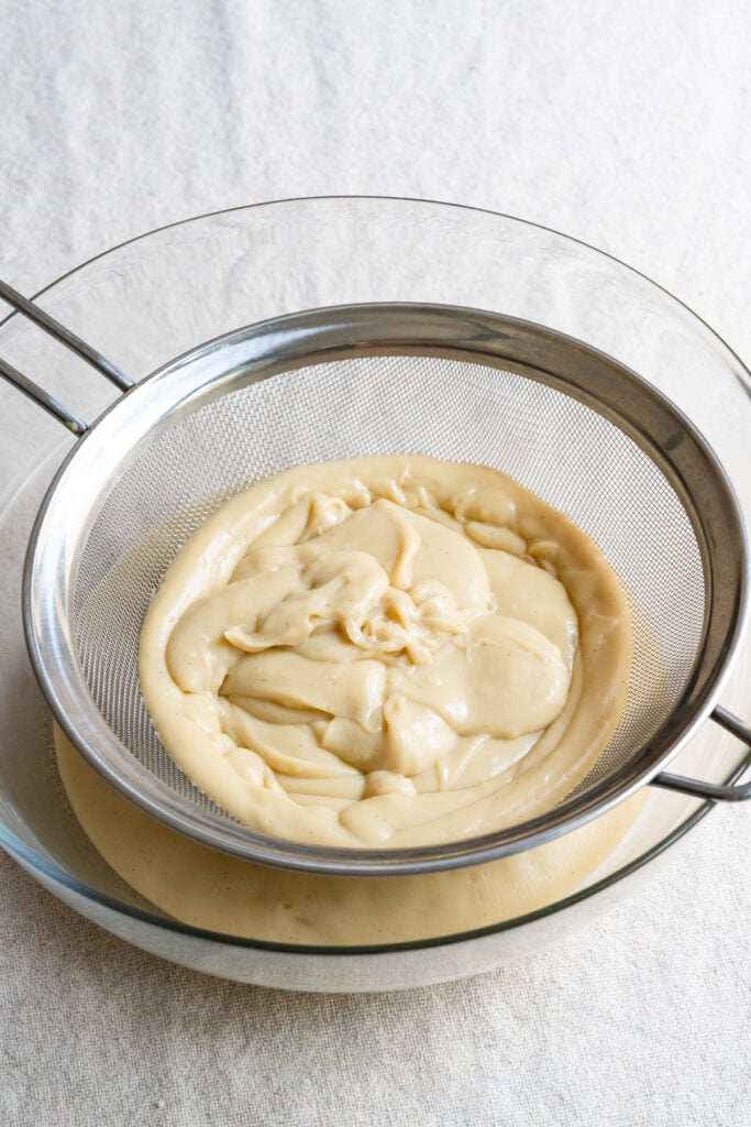 Pastry cream in a metal sieve in a glass bowl.