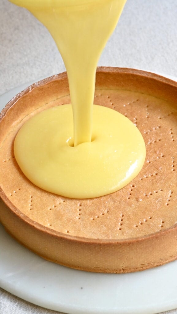 Lemon curd being poured into a baked tart shell.