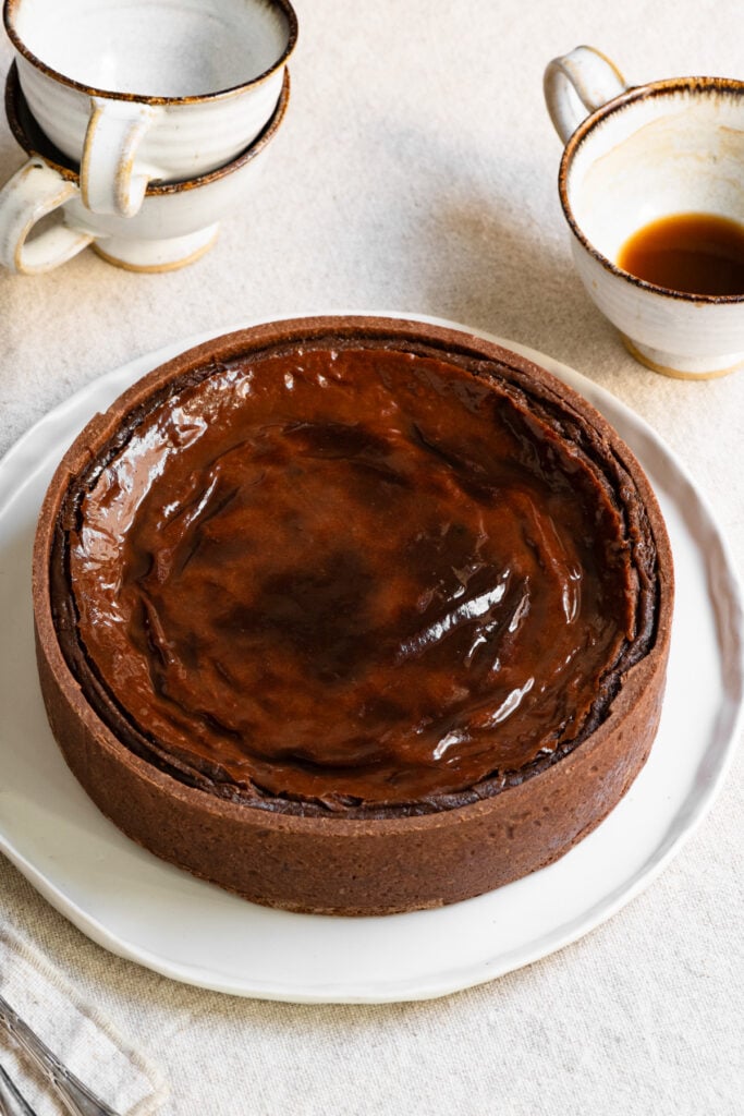 Baked chocolate French flan on a plate next to coffee mugs.