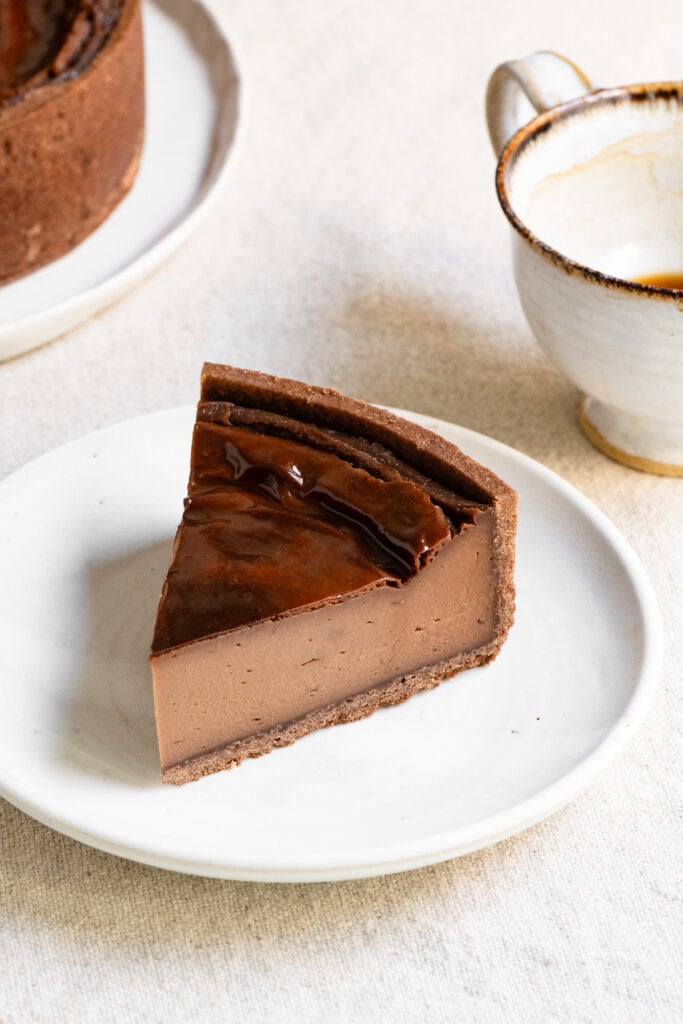 Slice of French chocolate flan on a plate next to a cup of coffee.