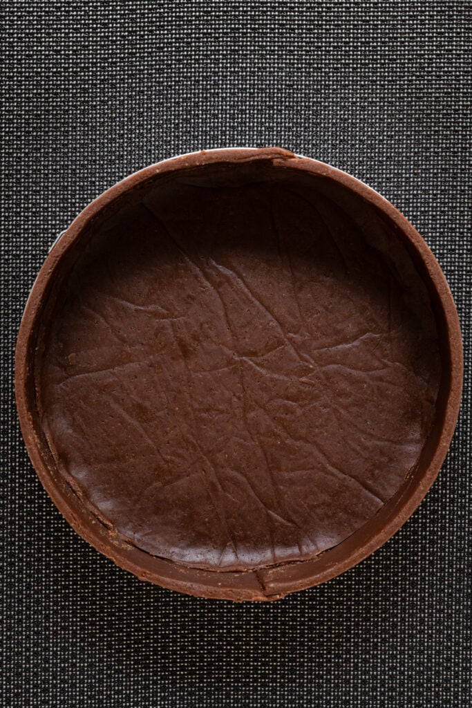Overhead of a chocolate pastry crust lined pastry ring on a baking mat.
