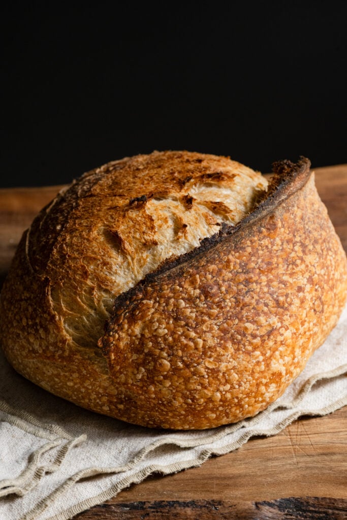 Baked loaf of sourdough bread on a linen napkin on a cutting board.