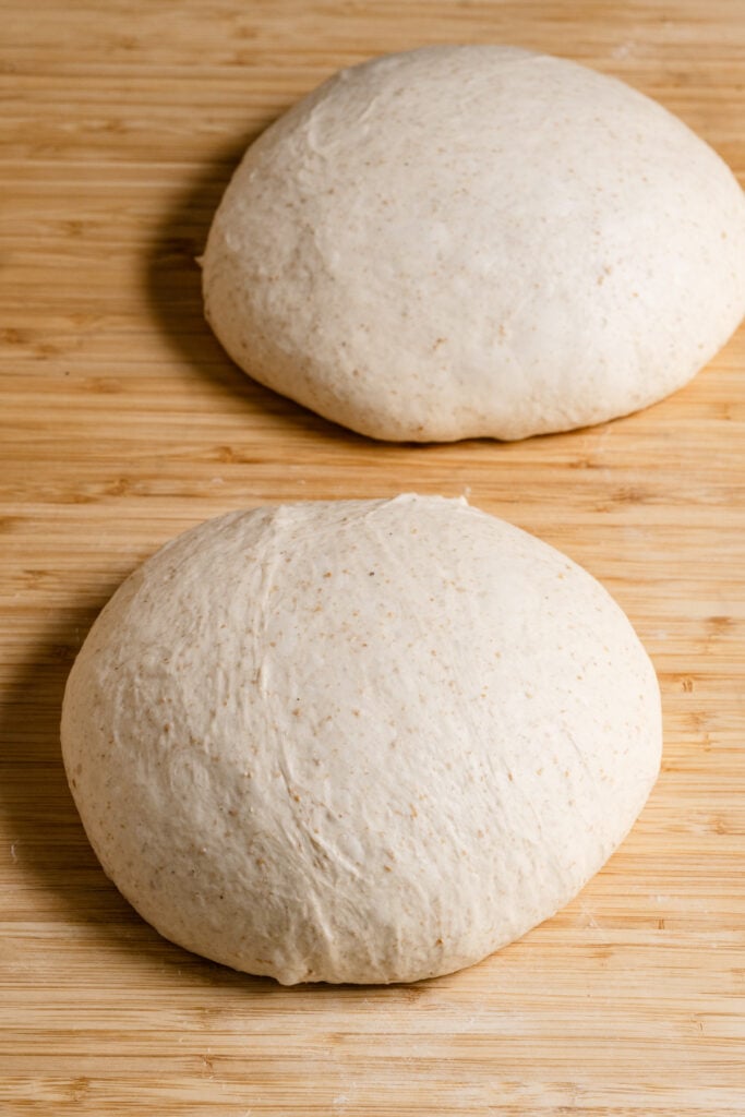 Two round balls of sourdough bread dough on wood counter top.