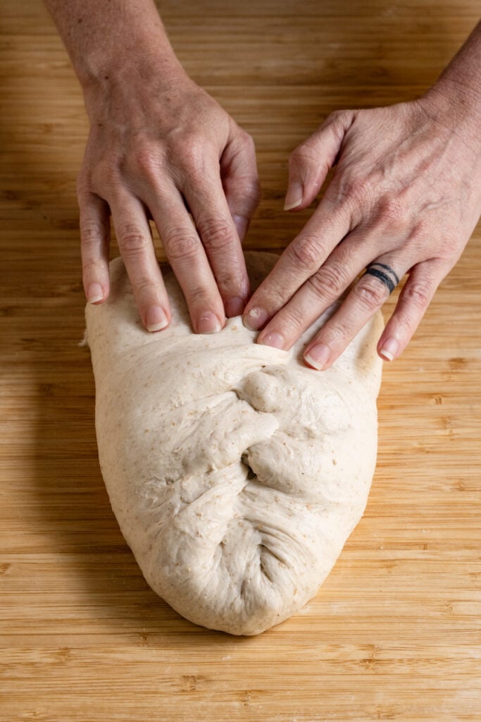 Hands folding sourdough into an oval.